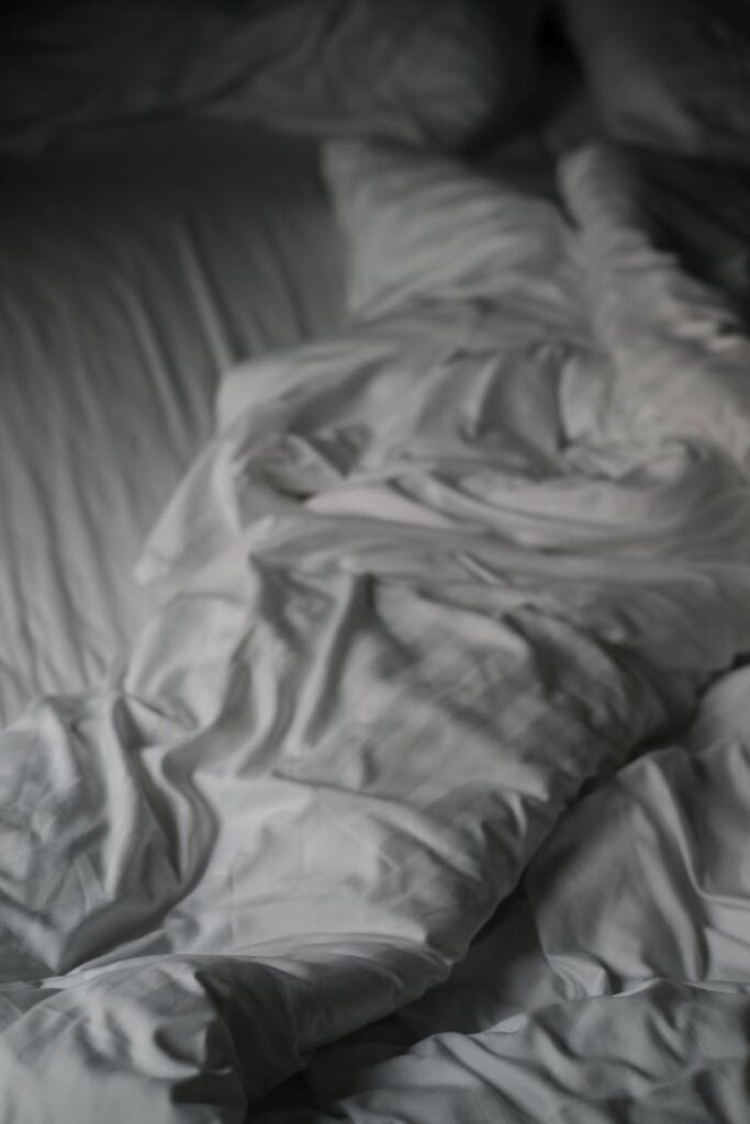 Detailed view of a soft white blanket with creases lying on a bed.