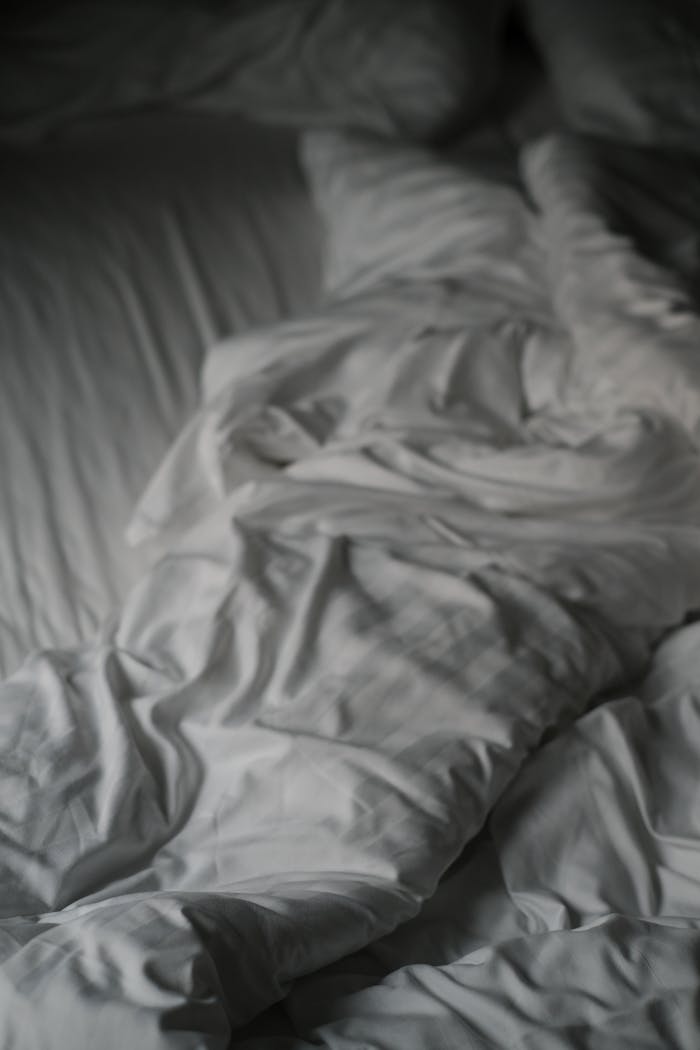Detailed view of a soft white blanket with creases lying on a bed.